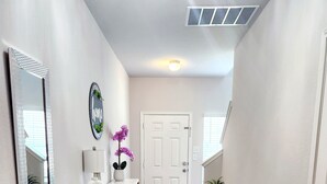A hallway with wooden flooring, a white door, a small table with a vase of flowers, and a wall-mounted mirror. - Lux New Beau;Houston;IAH Airport;Dtown;Woodlands;Spring;NRG World Cup Std;HotTub (Houston)