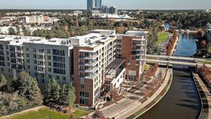 A multi-story building with a modern architectural design, featuring balconies and a river running alongside. - Lux New Beau;Houston;IAH Airport;Dtown;Woodlands;Spring;NRG World Cup Std;HotTub (Houston)