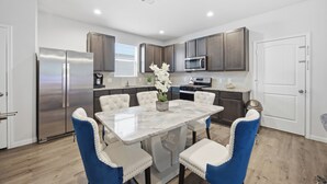 A modern kitchen with a stainless steel refrigerator, a microwave, and a dining area with a marble table and blue chairs. - Lux New Beau;Houston;IAH Airport;Dtown;Woodlands;Spring;NRG World Cup Std;HotTub (Houston)