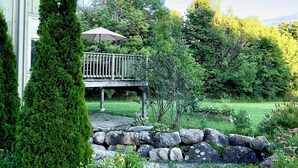 Una casa con un patio de piedra, una terraza de madera y un jardín bien cuidado con rocas y follaje.