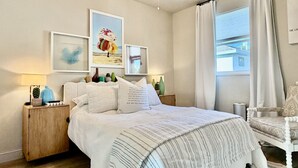 A bedroom with a bed, nightstands, a chair, and artwork on the walls.