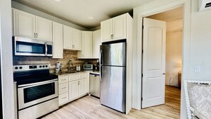 A modern kitchen with white cabinets, stainless steel appliances, and a wooden floor.