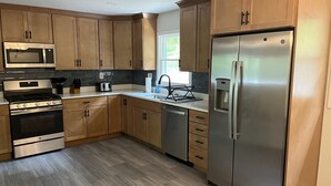 A modern kitchen with wooden cabinets, stainless steel appliances, and a grey tiled backsplash. - River Perch on the Cacapon: private home on 27 acres and 1200 ft of riverfront (Yellow Spring)