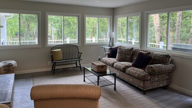 A spacious living room with large windows, a patterned sofa, a small table, and a chair. - River Perch on the Cacapon: private home on 27 acres and 1200 ft of riverfront (Yellow Spring)