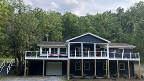 A two-story house with a covered front porch and a garage. - River Perch on the Cacapon: private home on 27 acres and 1200 ft of riverfront (Yellow Spring)