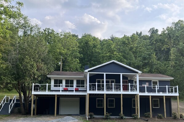 A two-story house with a covered front porch and a garage. - River Perch on the Cacapon: private home on 27 acres and 1200 ft of riverfront (Yellow Spring)