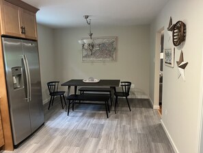 A kitchen with a stainless steel refrigerator, a dark wooden table with four chairs, and a wall-mounted light fixture. - River Perch on the Cacapon: private home on 27 acres and 1200 ft of riverfront (Yellow Spring)