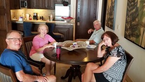 Un grupo de personas sentadas alrededor de una mesa redonda en una habitación con cocina al fondo.