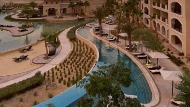 Un resort con varias piscinas, un edificio grande con balcones y vistas al atardecer.