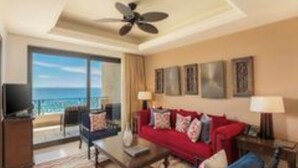Una habitación de hotel con sofá rojo, una mesa de centro, televisión y balcón con vista al océano.