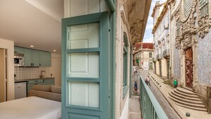 Un couloir étroit avec un balcon donnant sur une rue bordée d’immeubles et un escalier.