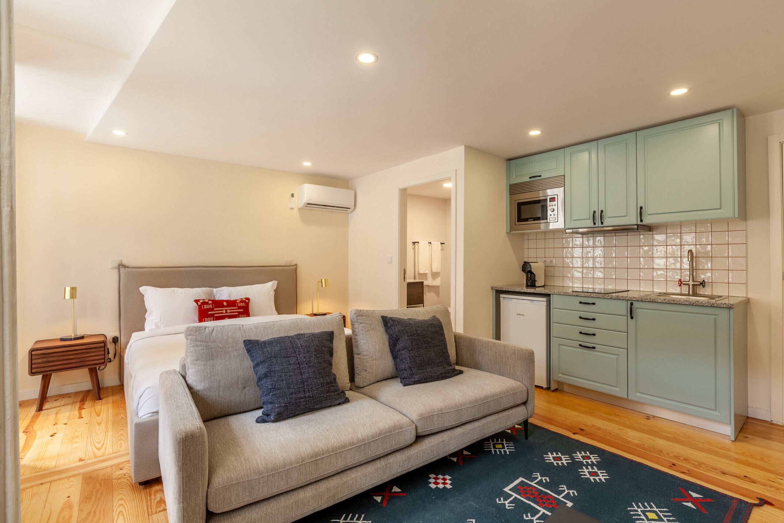 Un espacio habitable compacto con cama, sofá, kitchenette y suelo de madera.