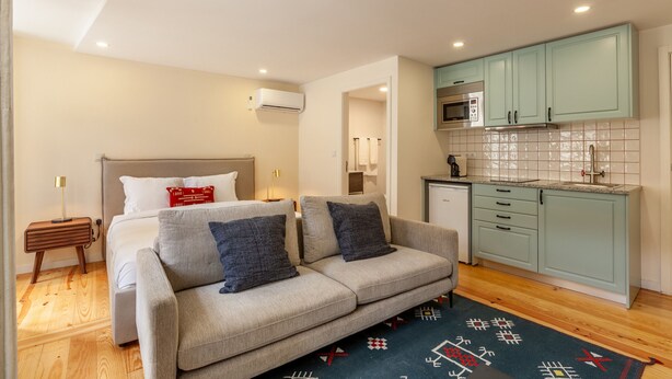 Un espacio habitable compacto con cama, sofá, kitchenette y suelo de madera.