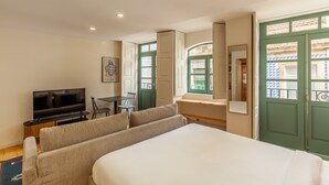 Une chambre d’hôtel avec un lit, une télévision, un canapé, un bureau et une fenêtre avec des volets verts.