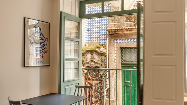 Une pièce avec une table et des chaises, une porte donnant sur un balcon d’où l’on peut admirer un immeuble à la façade carrelée.