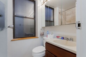 Bathroom features a toilet, sink, and mirror, with a window for natural light and toiletries on the counter.