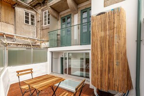 Ein Balkon mit Holztisch und -stühlen, einer Glastür und einem Bambus Sichtschutz.