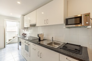 A modern kitchen with white cabinets, a stainless steel sink, a microwave, and a black countertop.