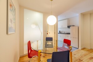 A modern dining area with a glass table and colorful chairs, a kitchen in the background, and a minimalist design.