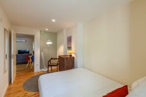 A modern hotel room with a large bed, a desk with a lamp, a chair, and a small table.