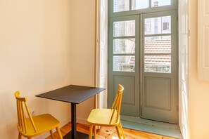 A room with a wooden floor, a black table, and two yellow chairs. A green door with windows is visible in the background. - Dasi Estudio C boutique apartment (Oporto)