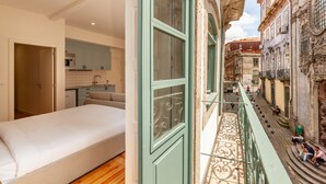 A bedroom with a bed, a kitchenette, and a balcony overlooking a street with buildings and people. - Dasi Estudio C boutique apartment (Oporto)