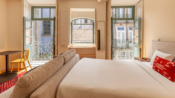 A hotel room with a large bed, a sofa, a small table, and a chair. There is a window with a view of a building outside. - Dasi Estudio C boutique apartment (Oporto)