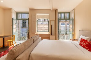 A hotel room with a large bed, a sofa, a small table, and a chair. There is a window with a view of a building outside. - Dasi Estudio C boutique apartment (Oporto)