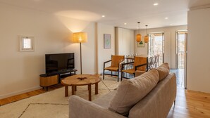 A modern living room with a sofa, a TV, a dining area with chairs and a table, and a lamp.
