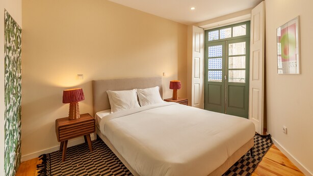 A bedroom with a large bed, two bedside tables with lamps, a green door, and a patterned rug.