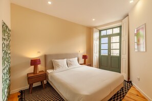 Une chambre avec un grand lit, deux tables de chevet avec des lampes, une porte verte et un tapis à motifs.