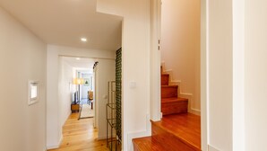 A hallway with wooden flooring, a staircase, and a door leading to another room.