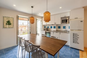 A modern kitchen with white cabinets, a stainless steel microwave, and a refrigerator. There is a dining table with chairs, and a window with a view of buildings. - Dasi Estudio E boutique apartment (Oporto)