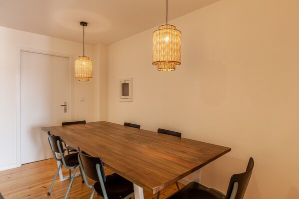 A spacious dining area with a long wooden table, black chairs, and two hanging wicker lamps.