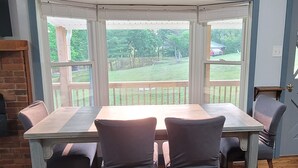 Zona pranzo con tavolo di legno e quattro sedie, camino in mattoni e vista sul giardino attraverso ampie finestre.