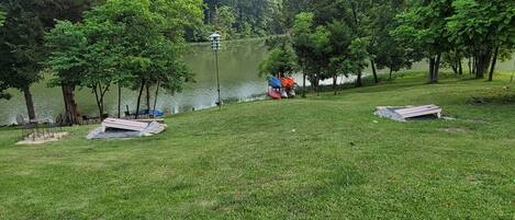 A grassy area with a lake, trees, and a gazebo-like structure.
