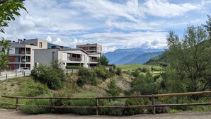 Un immeuble moderne à plusieurs étages, doté de balcons, entouré d’une végétation luxuriante et avec des montagnes en toile de fond.
