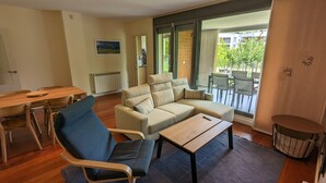 Un salon comprenant un canapé, une table à manger, des chaises, un radiateur et une vue sur un espace extérieur aménagé avec des chaises et une table, accessible par une porte vitrée.