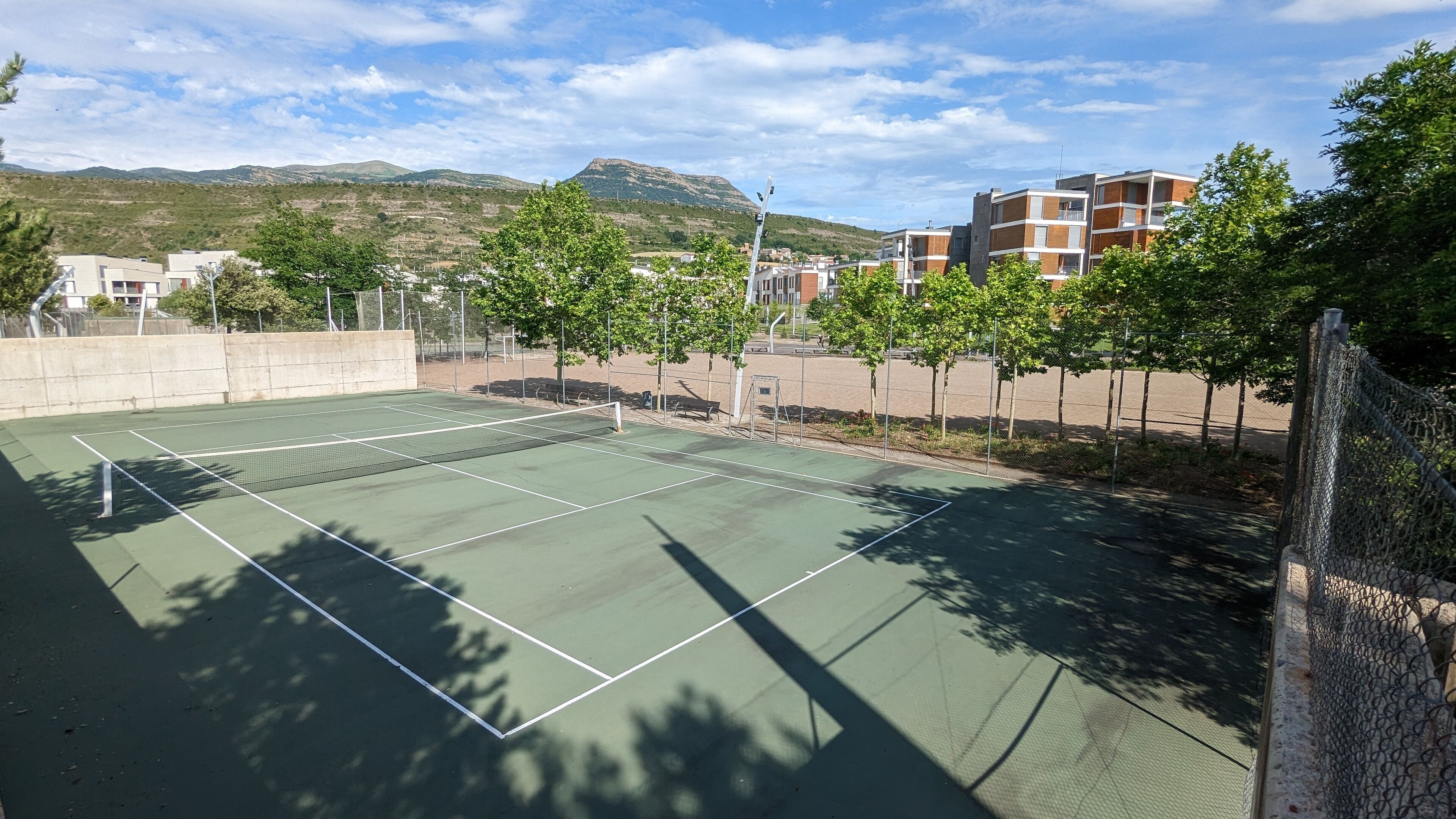 Una cancha de tenis con una red, rodeada de árboles y edificios.