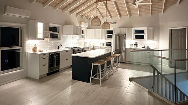 Een moderne keuken met een groot eiland, witte kasten en een houten plafond.