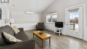 Un salon avec un canapé, une table basse, un téléviseur et une porte donnant sur l’extérieur.