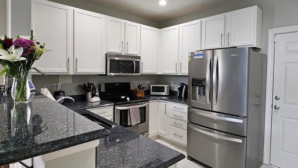 A modern kitchen with white cabinets, a stainless steel refrigerator, a microwave, and a gas stove. - Comfortable, covenient, quaint (Winston-Salem)