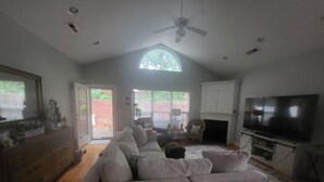 A living room with a grey sofa, a flat-screen TV, a fireplace, and a ceiling fan. - Comfortable, covenient, quaint (Winston-Salem)