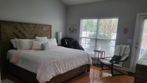 A bedroom with a large bed, a wooden headboard, a chair, and a window with blinds. - Comfortable, covenient, quaint (Winston-Salem)