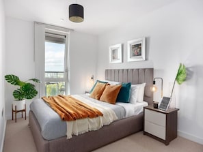 Relax in this serene bedroom with a large bed, bedside table, and a potted plant by the window.