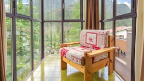 A room with large windows offering a mountain view, a wooden bed with a patterned blanket, and a green tiled floor. - Appartamento Antermoia by Interhome (Canazei)