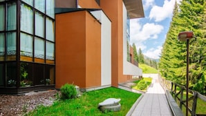 A modern building with large windows, a well-maintained lawn, and a pathway leading to a wooden fence. - Appartamento Antermoia by Interhome (Canazei)
