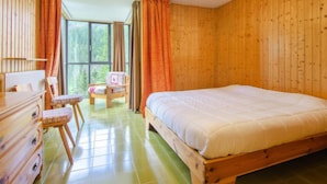 A wooden-paneled room with a large bed, a dresser, a chair, and a window with curtains. - Appartamento Antermoia by Interhome (Canazei)