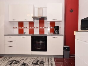 Una cocina moderna con armarios blancos, un horno negro y un salpicadero rojo y blanco.
