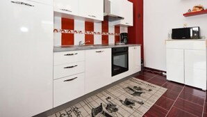 A modern kitchen with white cabinets, red accents, a built-in oven, and a microwave on a small countertop. - Zalazak Sunca by Interhome (Novigrad (Zadar))